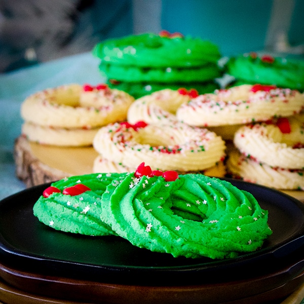 A tray stacked with Spritz cookies shaped like Christmas wreaths.