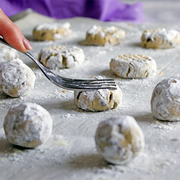 Making a grid pattern on balls of pecan sand tart cookie dough before baking.