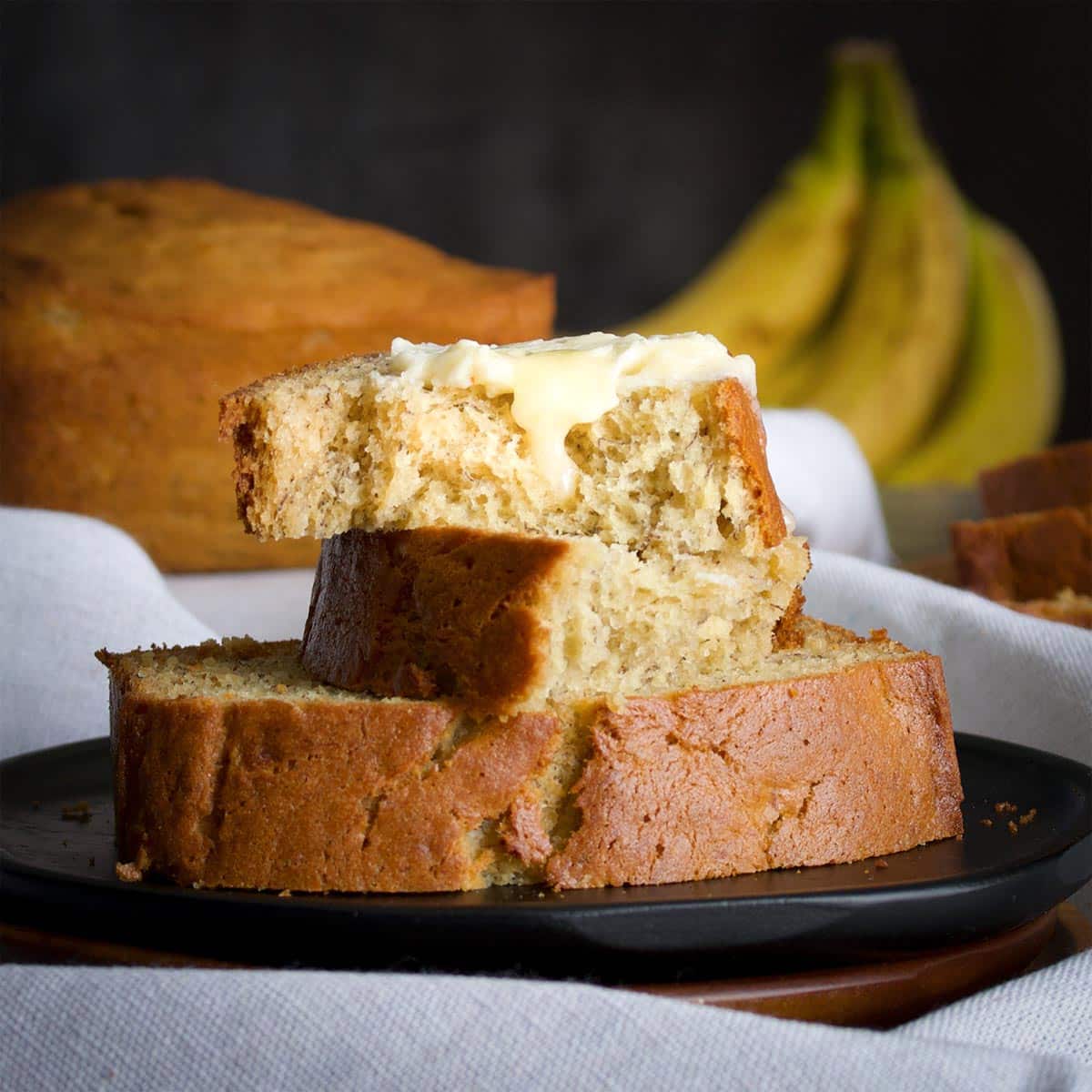 Several slices of banana bread on a plate topped with butter.
