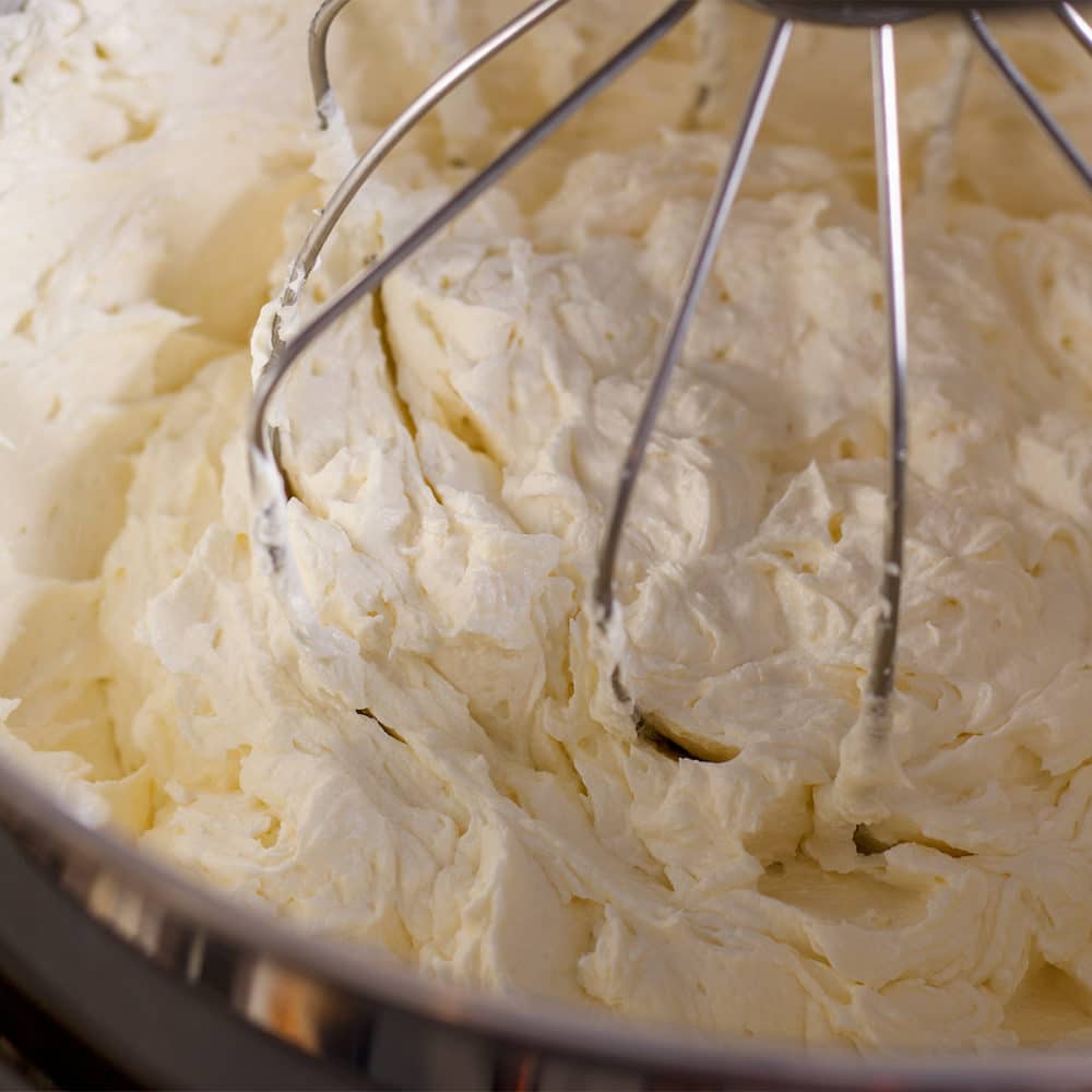 A photo looking down into the bowl of an electric stand mixer so you can see the thickened consistency of cream cheese buttercream after powdered sugar has been added.