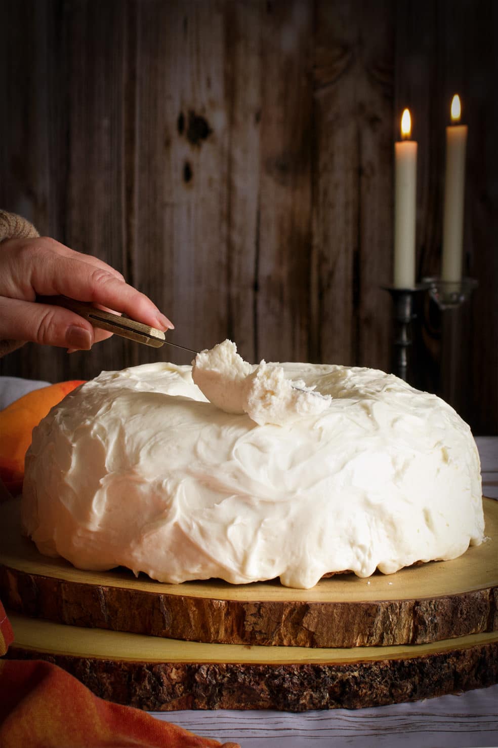 Someone using an icing spatula to spread cream cheese buttercream onto a bundt cake.