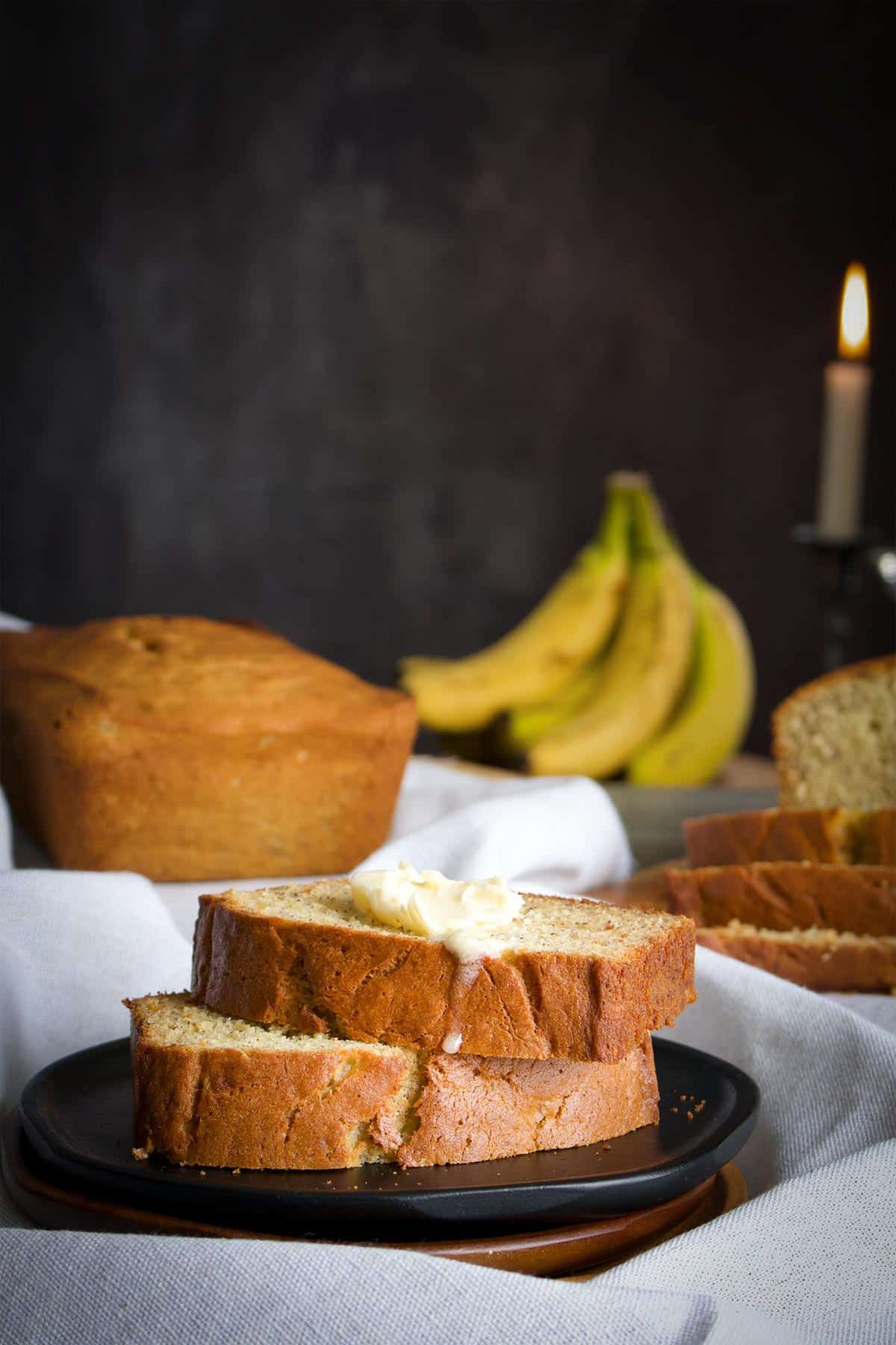 Two slices of homemade banana bread on a plate topped with butter that's melting down the sides of the bread.