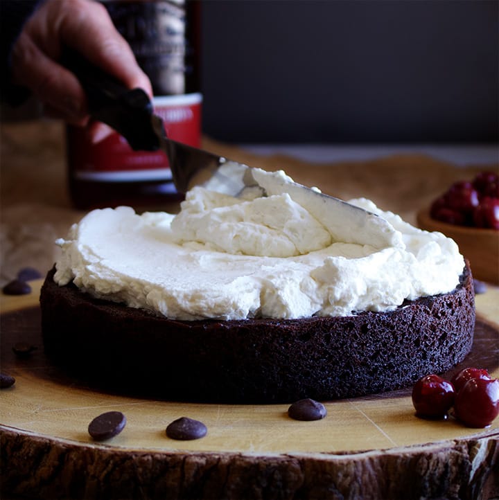 Spreading whipped cream onto a layer of Devil's Food Cake to make Black Forest Cake