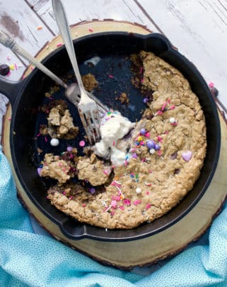 A half eaten skillet cookie with chocolate chips and oatmeal, ice cream and sprinkles.