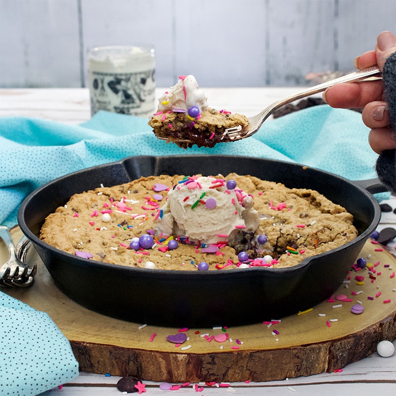 Taking a bite of a big chocolate chip oatmeal skillet cookie with ice cream and sprinkles.