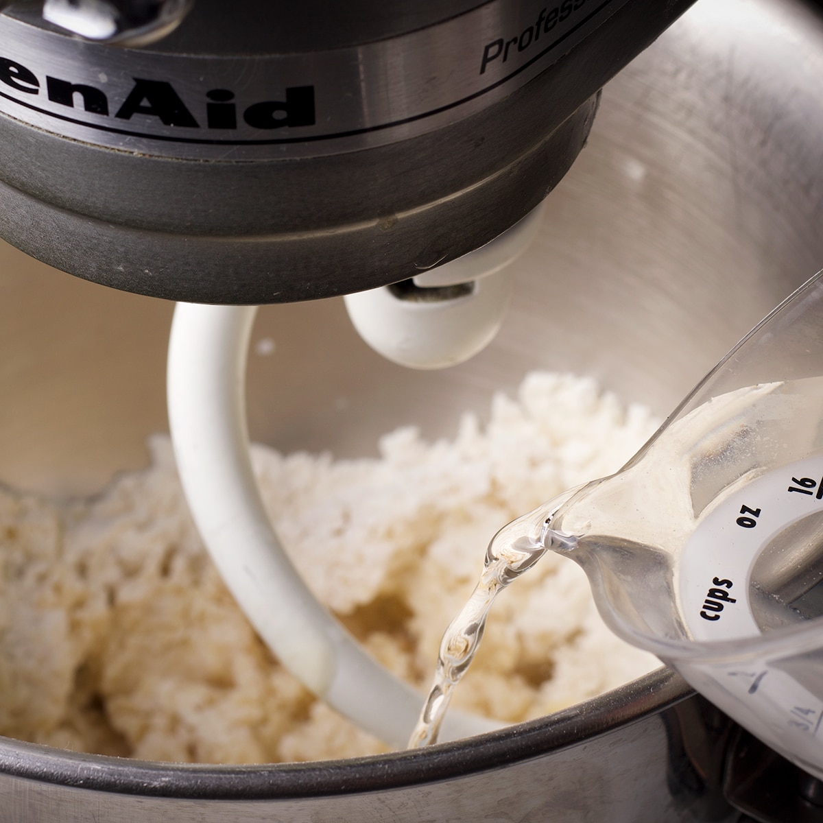 Pouring warm water into the bowl of a stand mixer while the mixer is running to make tortilla dough.