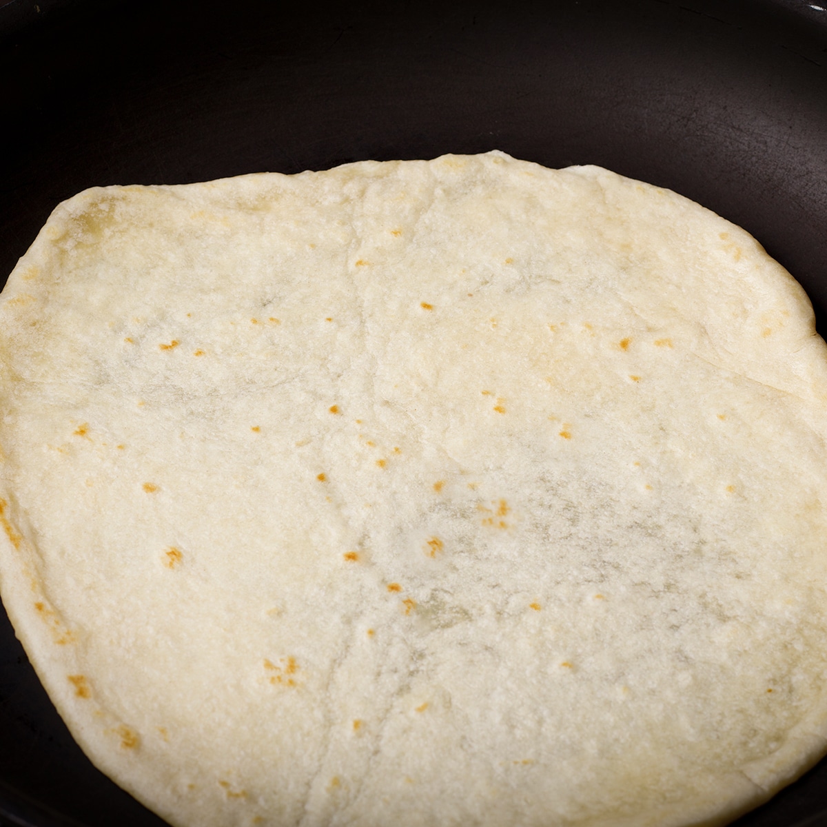 A homemade flour tortilla cooking in a skillet.