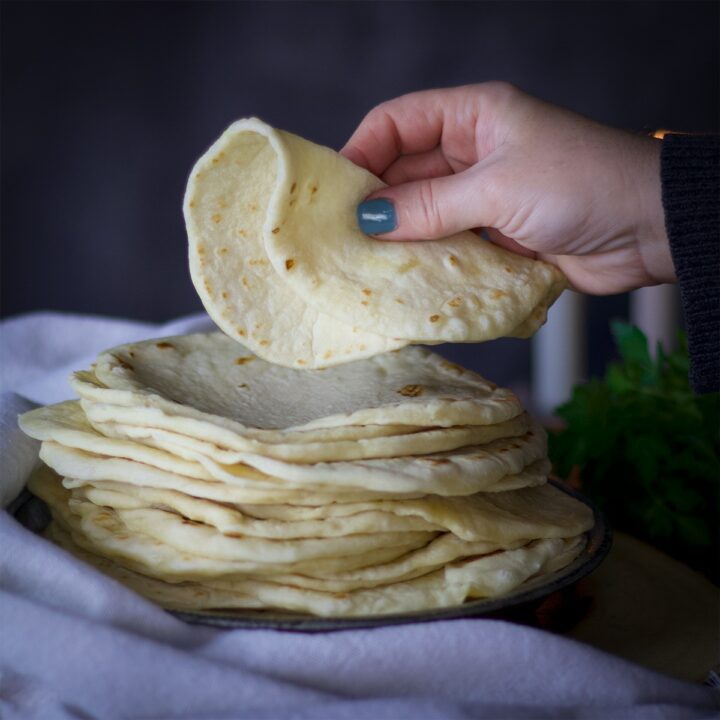 Someone lifting a homemade flour tortillas from a large stack of tortillas.