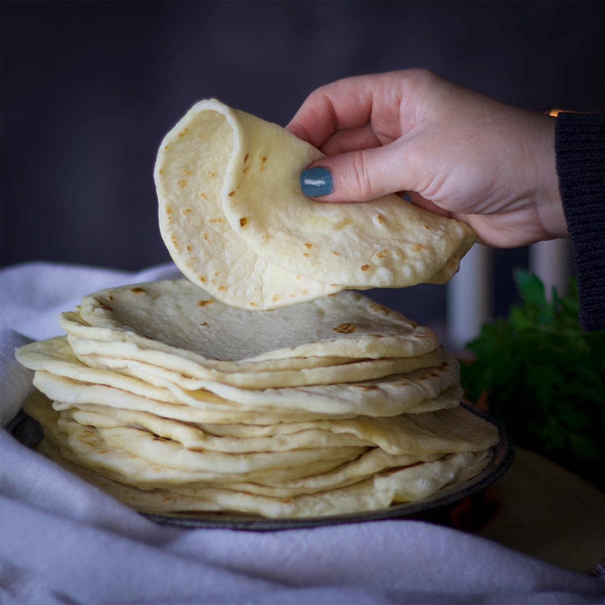 Someone lifting a homemade flour tortillas from a large stack of tortillas.