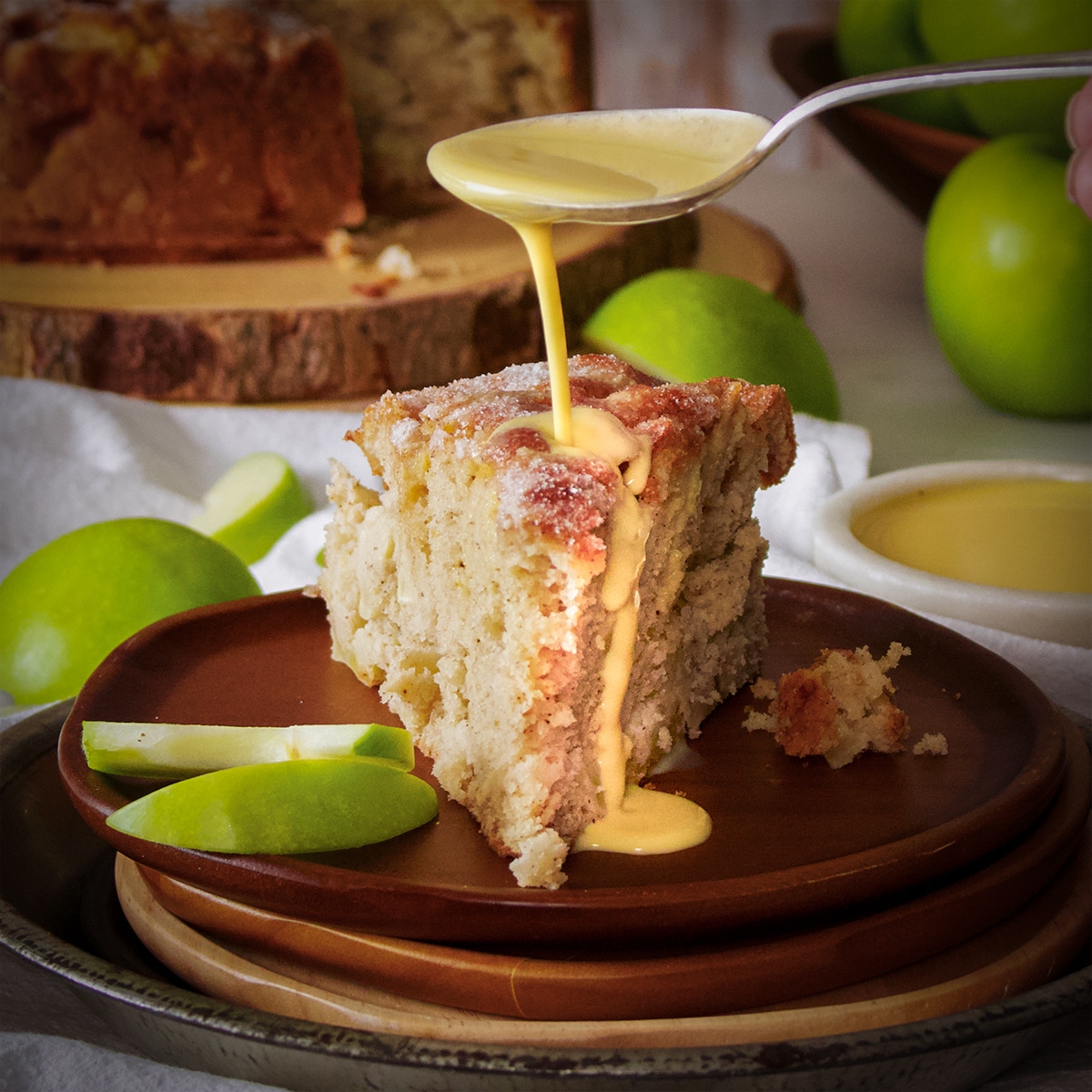 Someone using a spoon to pour custard sauce over a slice of Irish Apple Cake.
