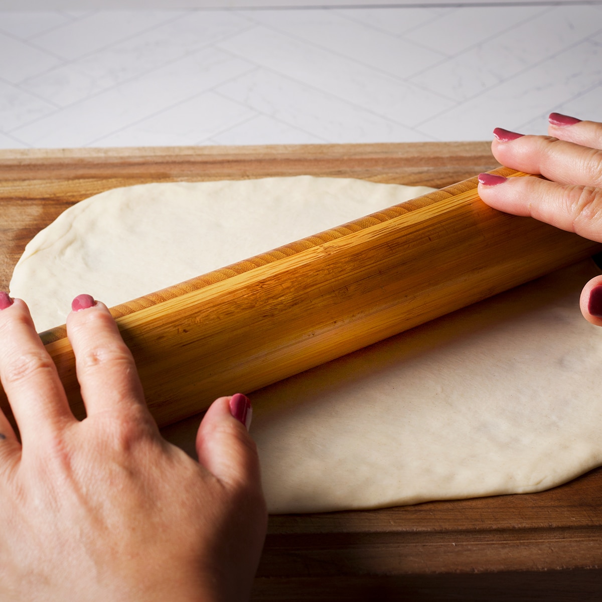 Someone using a wood rolling pin to roll out tortilla dough.