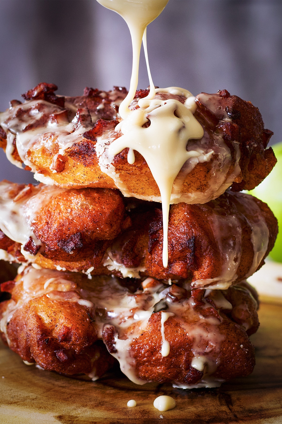 A stack of three apple fritters with maple glaze dripping down the side.