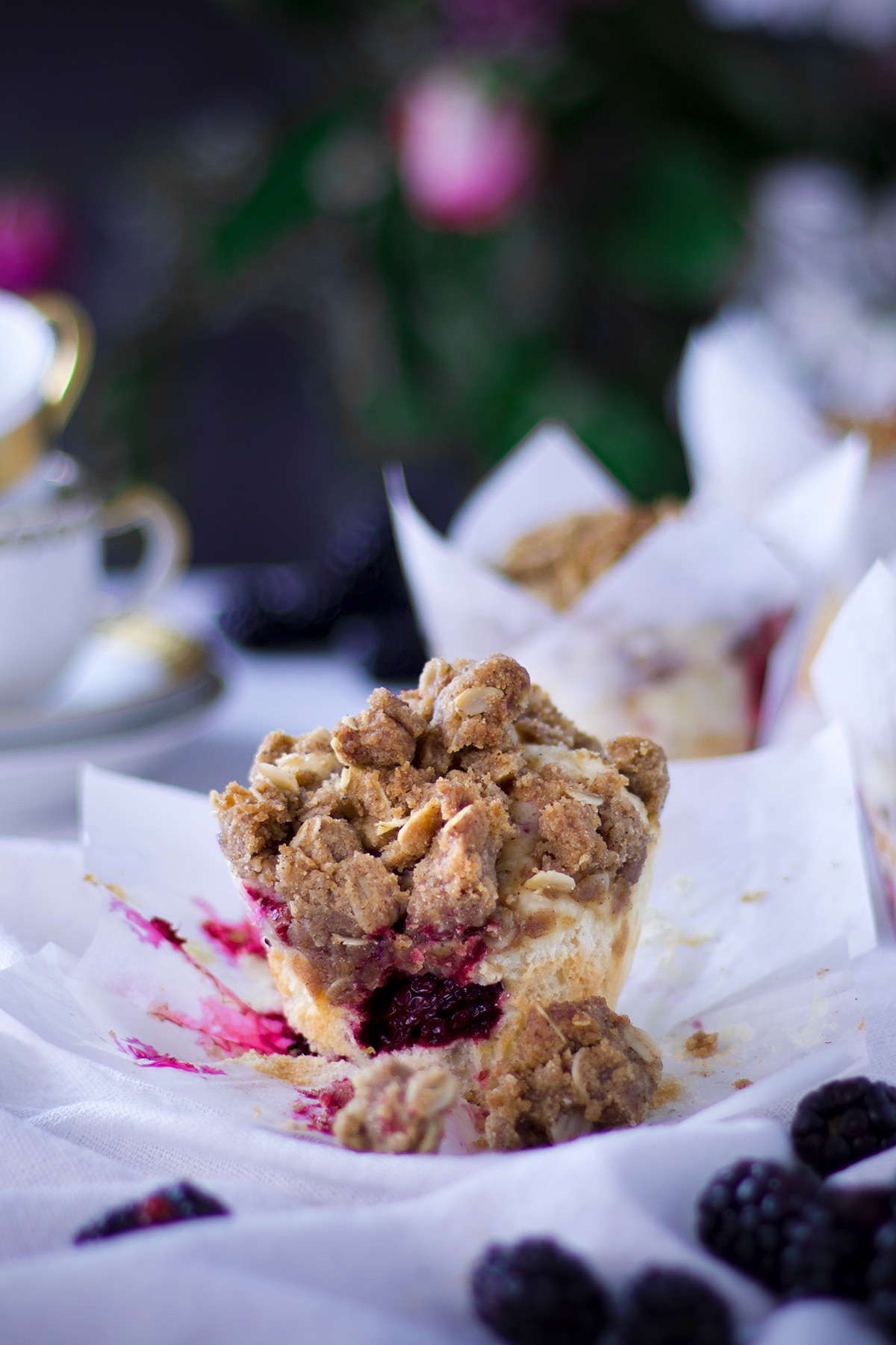 A mixed berry muffin with streusel on a white plate with more muffins and fresh berries surrounding it. 