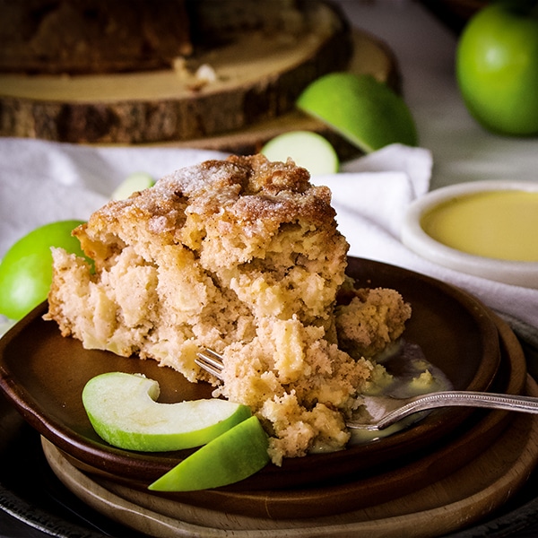 A slice of Irish Apple Cake with Custard Sauce on a plate with some sliced apples and a fork.