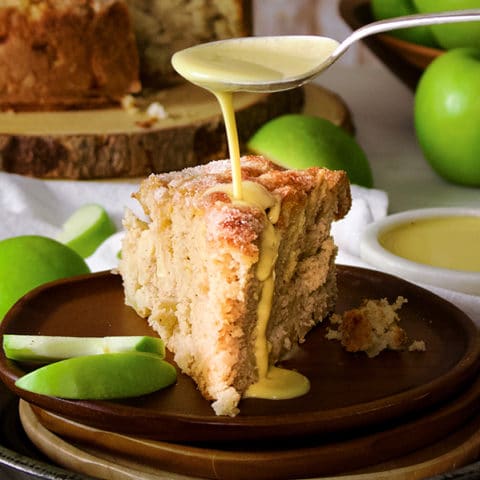 Drizzling a spoonful of custard sauce over a slice of Irish Apple Cake.