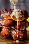 Someone drizzling maple glaze over a stack of three homemade apple fritters.