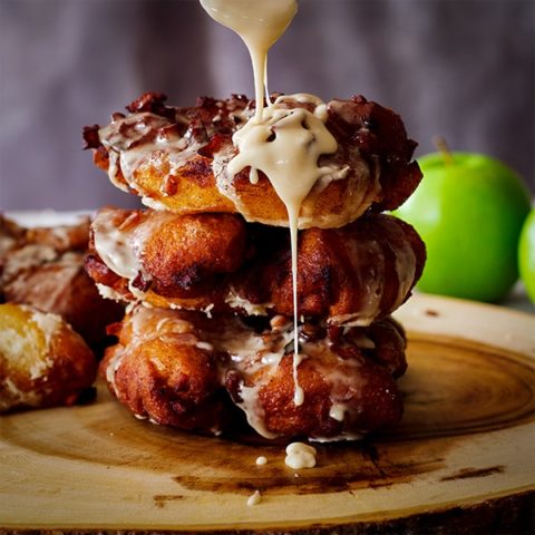 Drizzling Maple Glaze over a stack of three homemade Apple Fritter Doughnuts