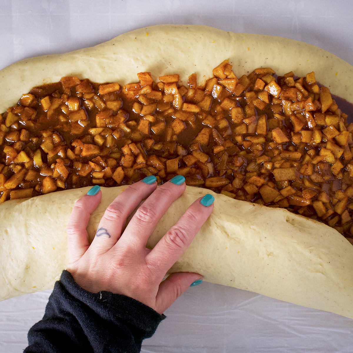 Someone using their hands to roll up a log of dough filled with apple fritter filling.