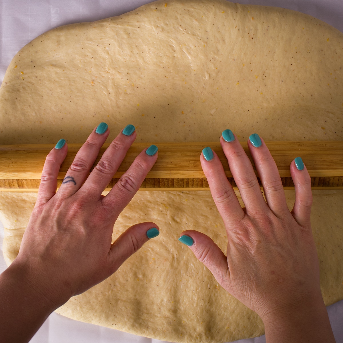 Someone using a wood rolling pin to roll out a rectangle of bread dough.