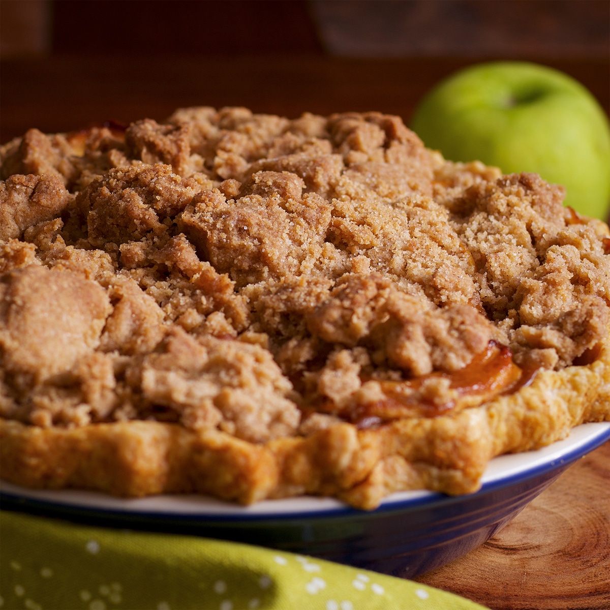 A freshly baked caramel apple pie with a crumb topping resting on a wood cutting board.