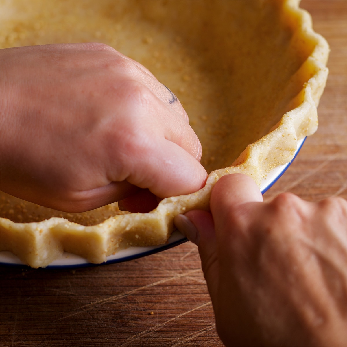 Someone using their fingers to crimp the edges of a pie crust inside a pie plate.