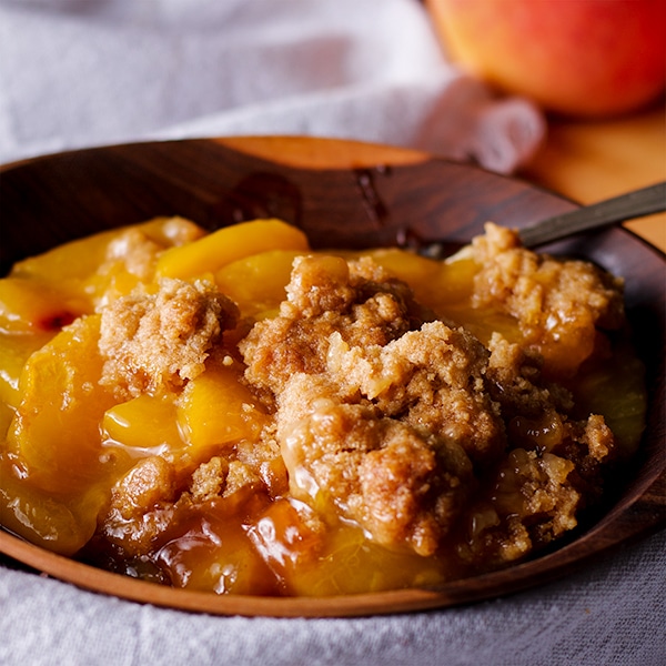 A bowl of peach cobbler with brown sugar cookie crust.