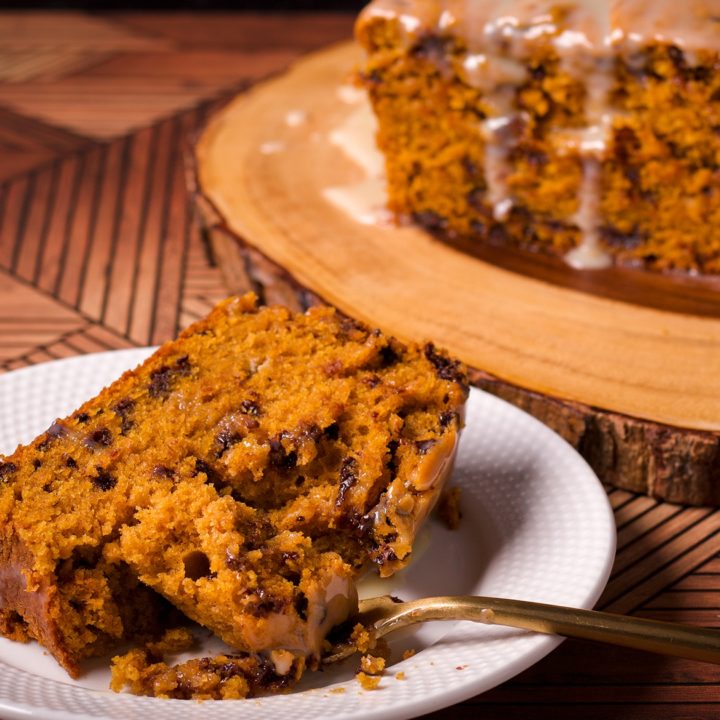 A slice of pumpkin chocolate chip bread on a white plate with a bite resting on a gold fork.