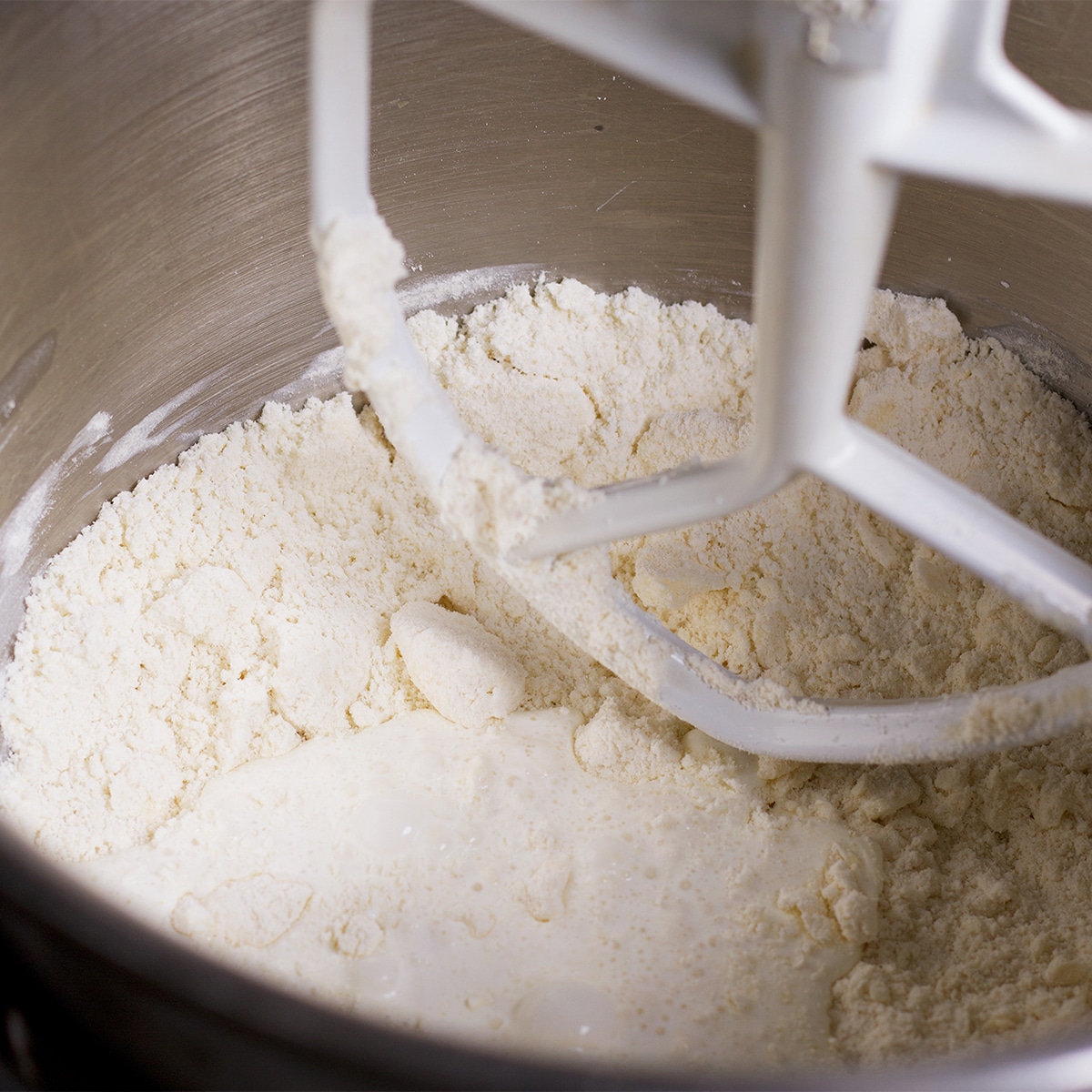 Adding cream to the flour and butter mixture as it mixes together in the bowl of a stand mixer.