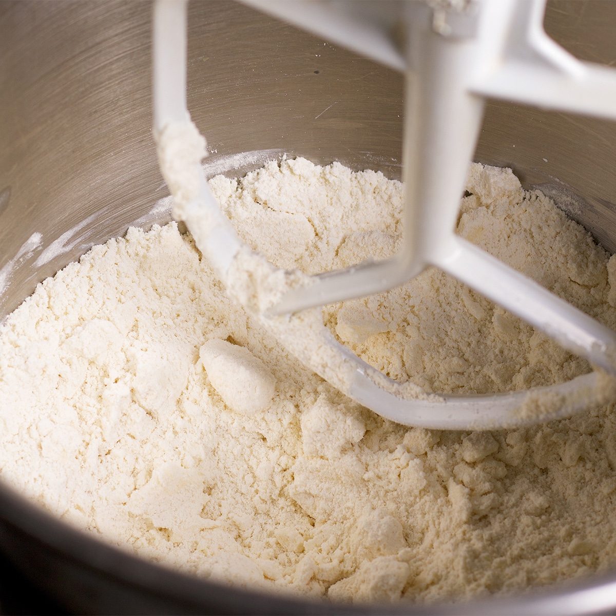 Looking down into the bowl of a stand mixer containing flour that's been mixed with cold butter.