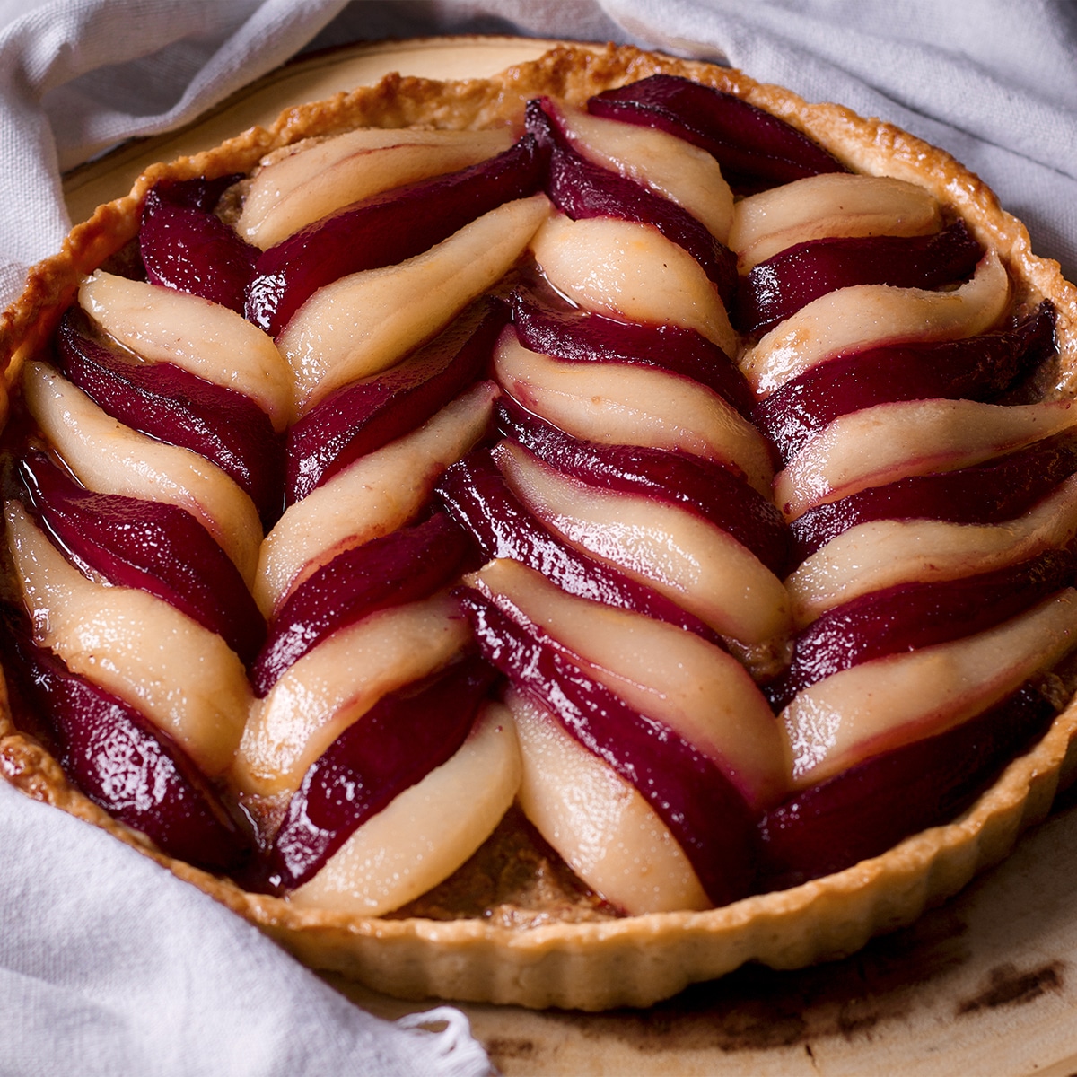 A poached pear and frangipane tart on a wood serving platter.