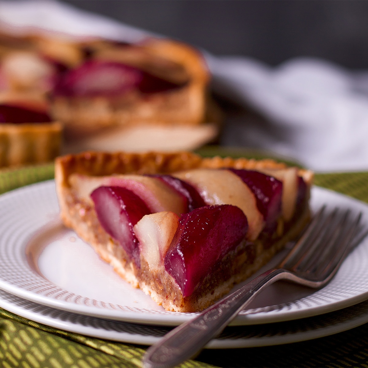 A slice of poached pear and frangipane tart on a white plate with a fork.