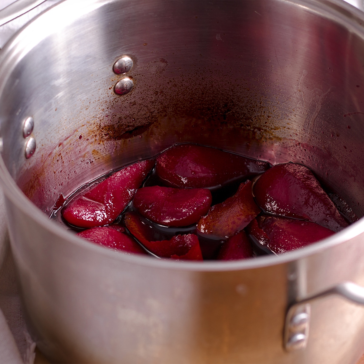 A saucepan containing pears poaching in red wine.