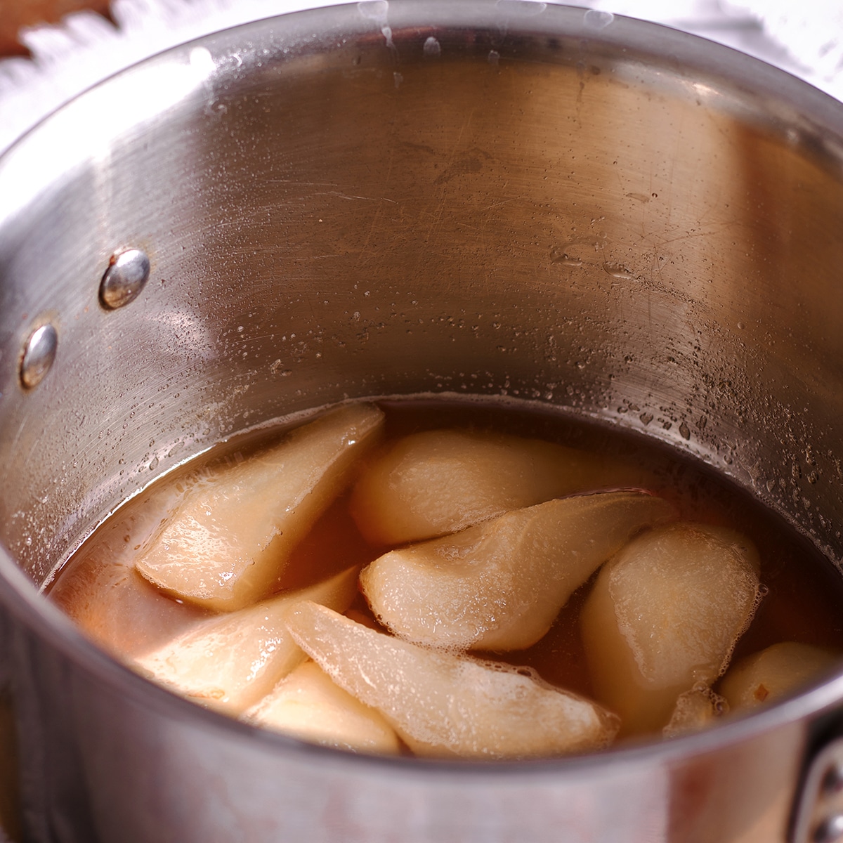 A saucepan containing white wine and sliced pears.