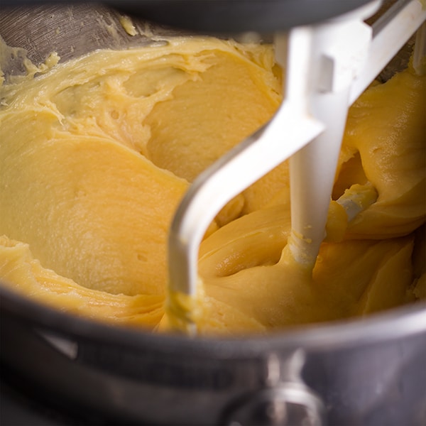 A photo looking down into the bowl of a standing mixer so you can see the mixer beating the eggs into choux pastry dough until it's thick and shiny.