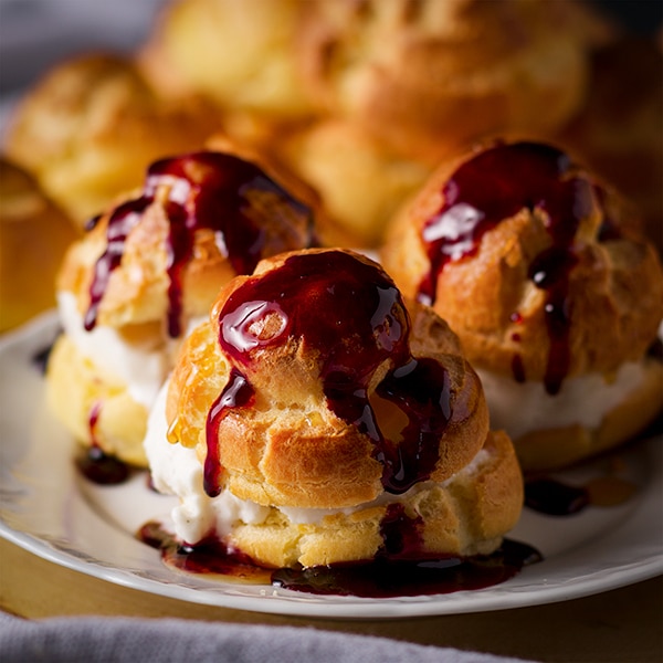 A plate of homemade profiteroles filled with vanilla ice cream and drizzled with sweet wine dessert sauce.