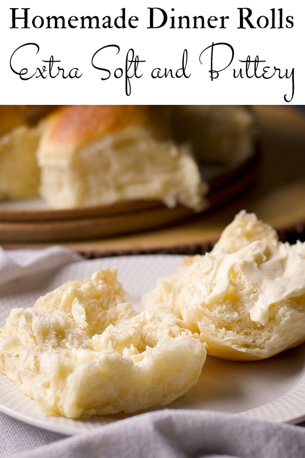 A homemade dinner roll on a plate, split in half and spread with butter.