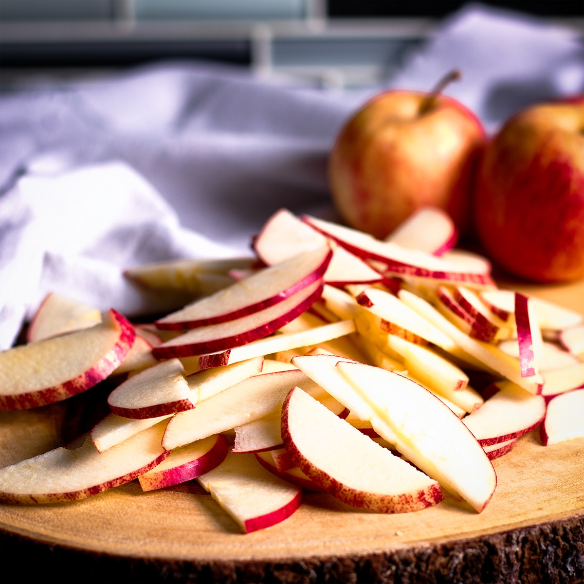 A pile of apple slices on a wood cutting board.