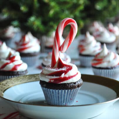 A mini chocolate peppermint cupcake decorated with a swirl of buttercream and a candy cane on a white plate.