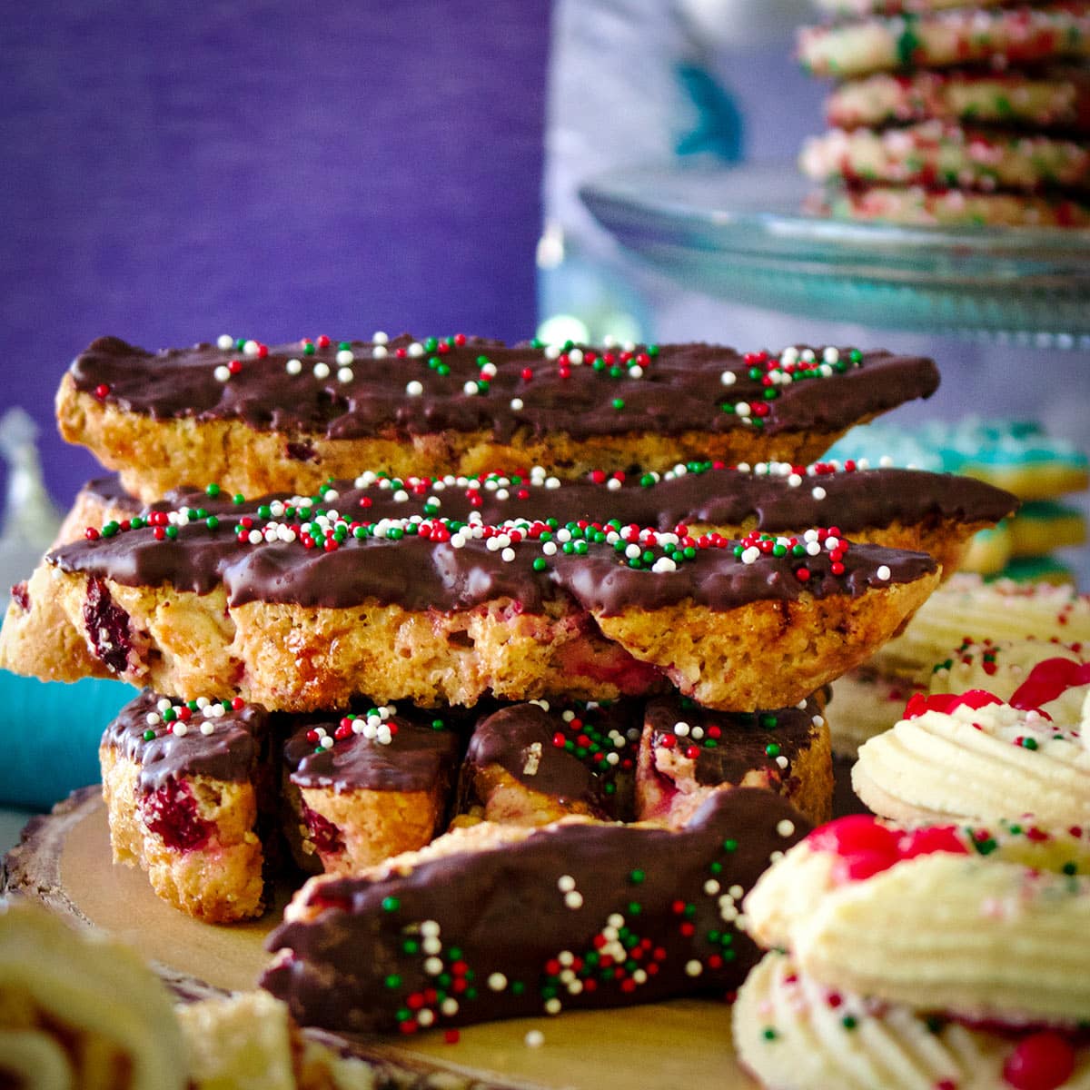 A wood tray piled high with several kinds of Christmas cookies including cranberry orange biscotti dipped in dark chocolate.