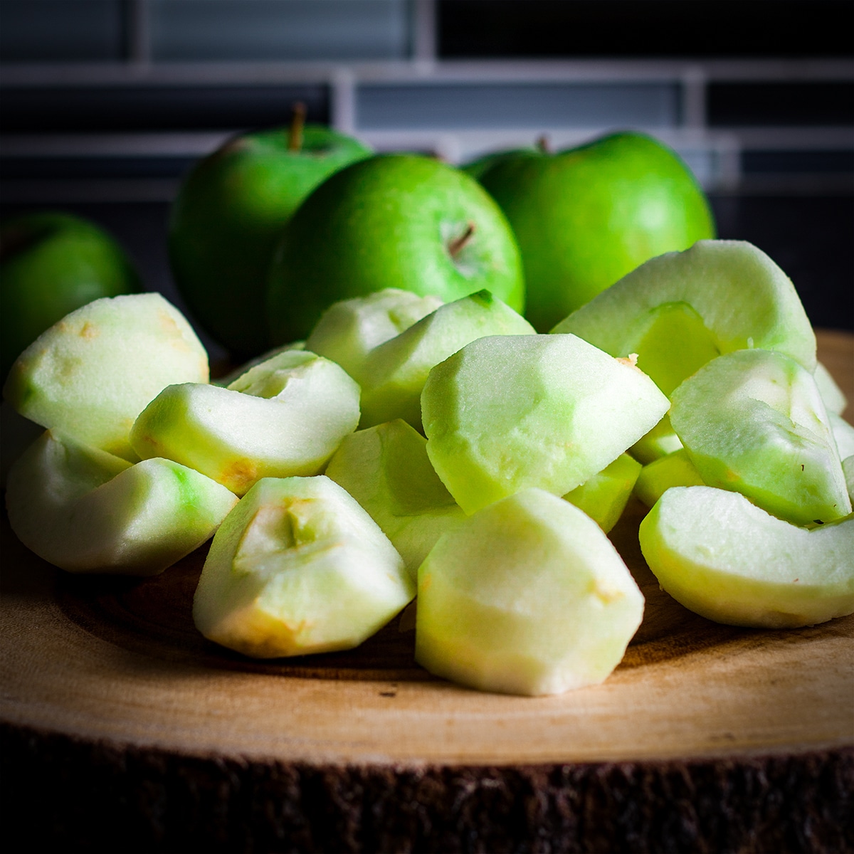 A pile of partially peeled and sliced green apples on a wood cutting board.