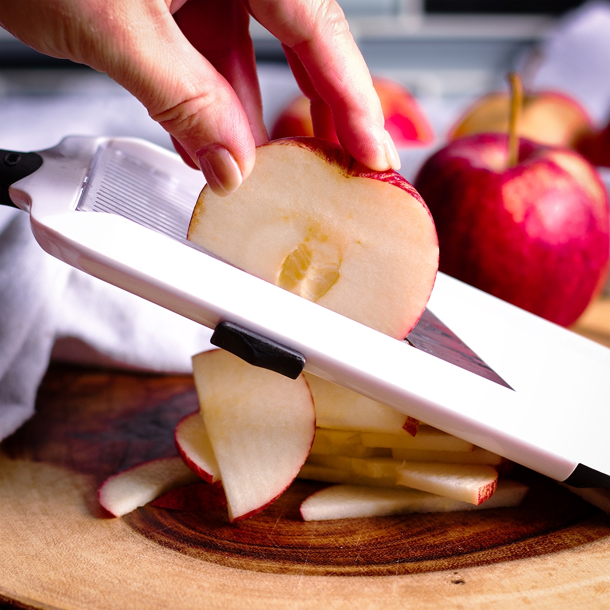 Someone using a mandolin to slice apples into thin slices.