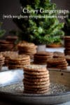Mini Gingerstap cookies stacked on a plate with more cookies and Christmas trees in the background