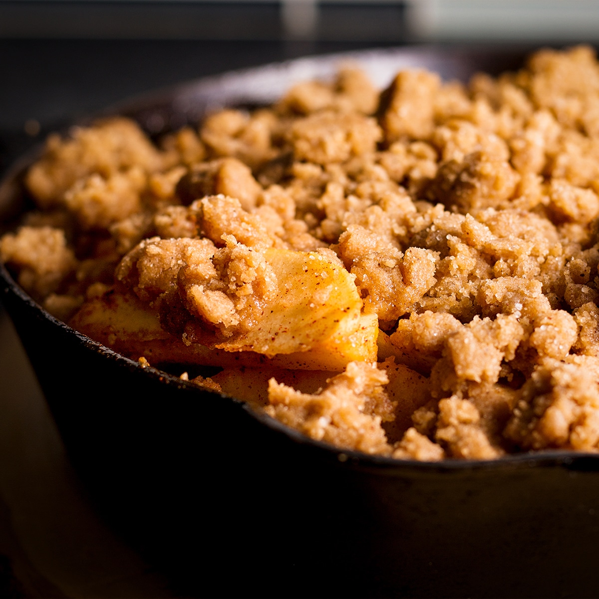 Someone lifting a spoonful of apple cobbler from a cast iron skillet.