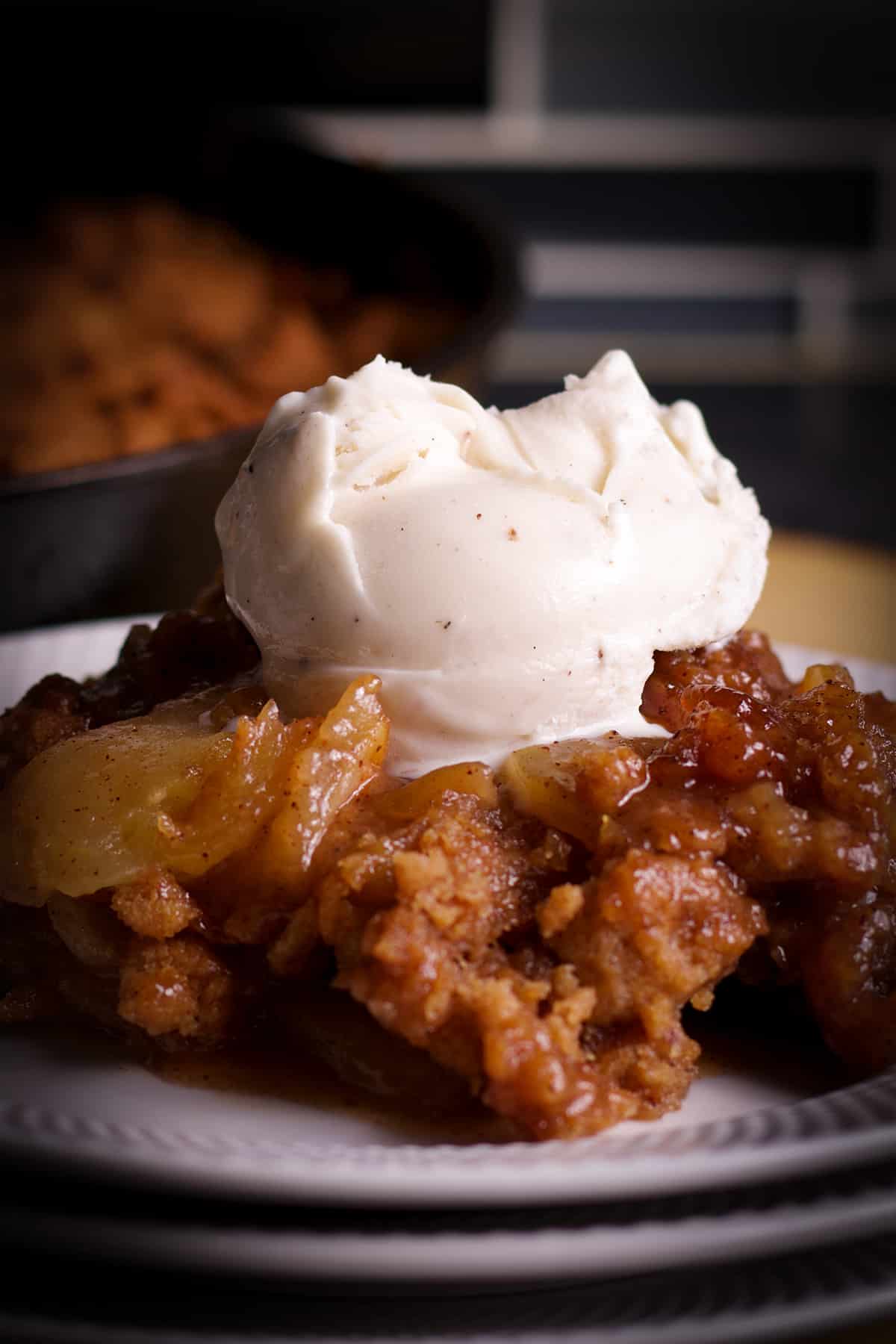 A serving of apple cobbler topped with vanilla ice cream on a white plate.