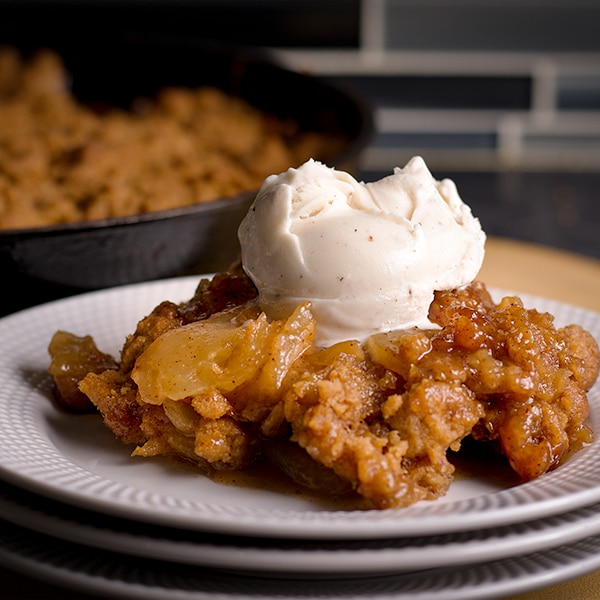 A serving of Apple Cobbler topped with a scoop of vanilla ice cream.