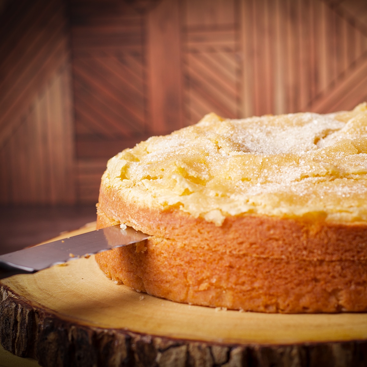 Someone using a serrated knife to cut an olive oil cake in half so it can be filled with mascarpone pastry cream.