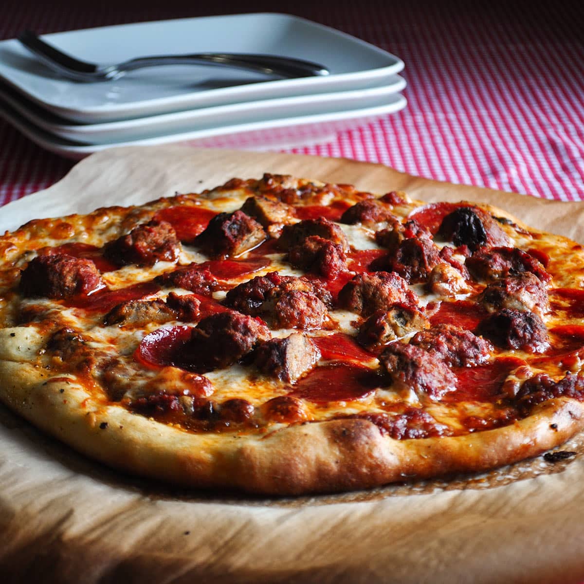 A homemade pepperoni and meatball pizza that's been baked on parchment paper.