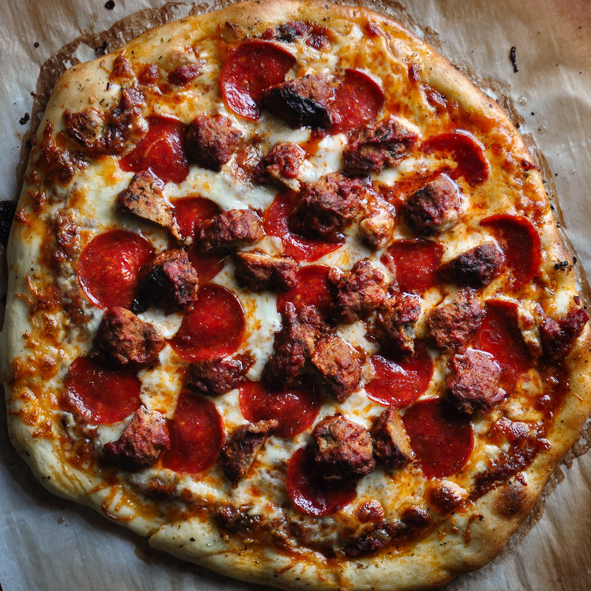 A homemade pepperoni and meatball pizza that's been baked on parchment paper. 