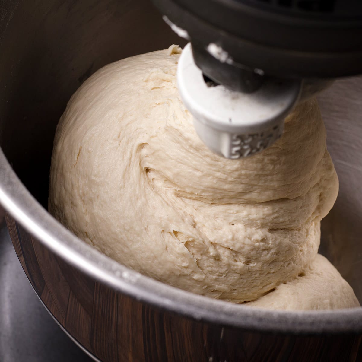 A KitchenAid stand mixer fitted with the dough hook, kneading pizza dough.