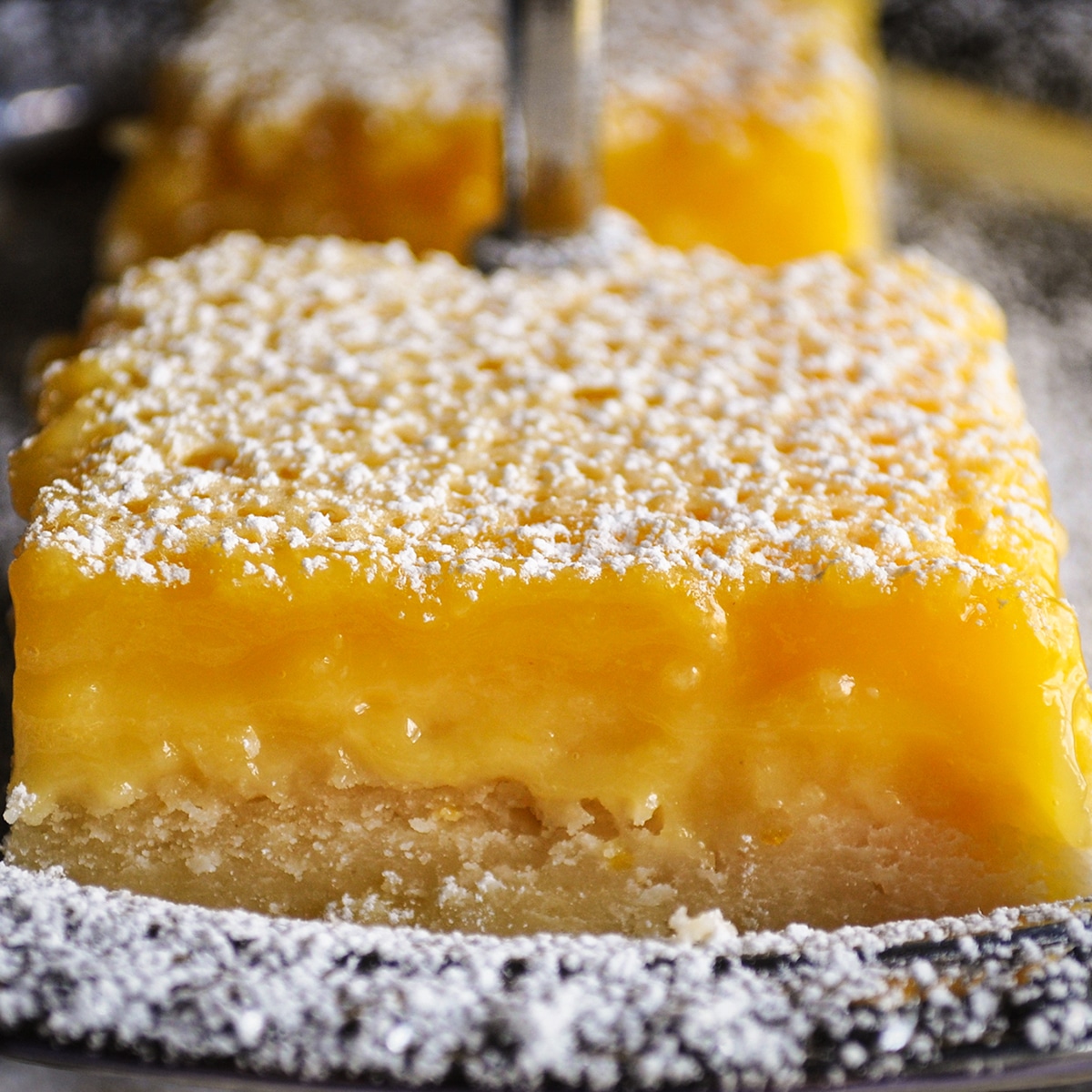 A lemon bar that's been sprinkled with powdered sugar resting on a silver platter.